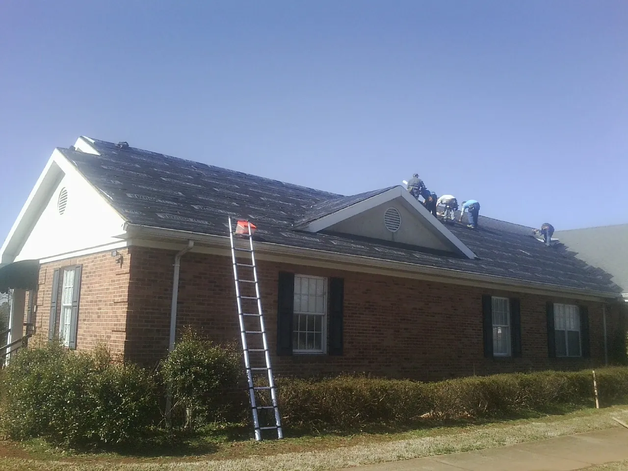 Crew tearing shingles off a brick ranch roof with a ladder set — Emergency Roof Repair work by our crew in Painesville