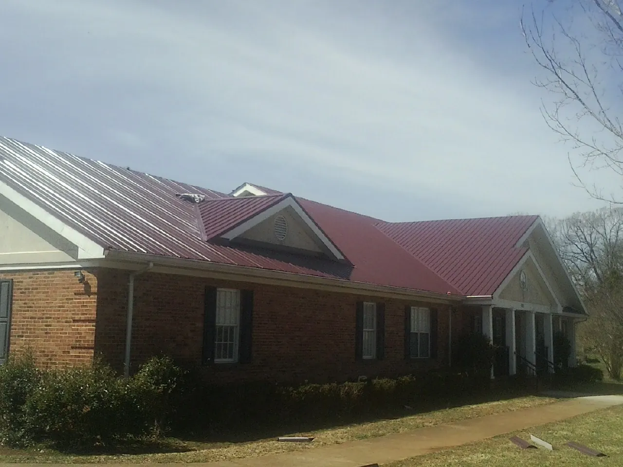 Red metal roof with gabled entries on a long brick building, from a Hail Damage Roof Repair job in Painesville