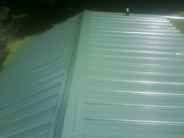 New green metal panels meeting at the ridge of a roof — Flat Roof Repair work by our crew in Painesville