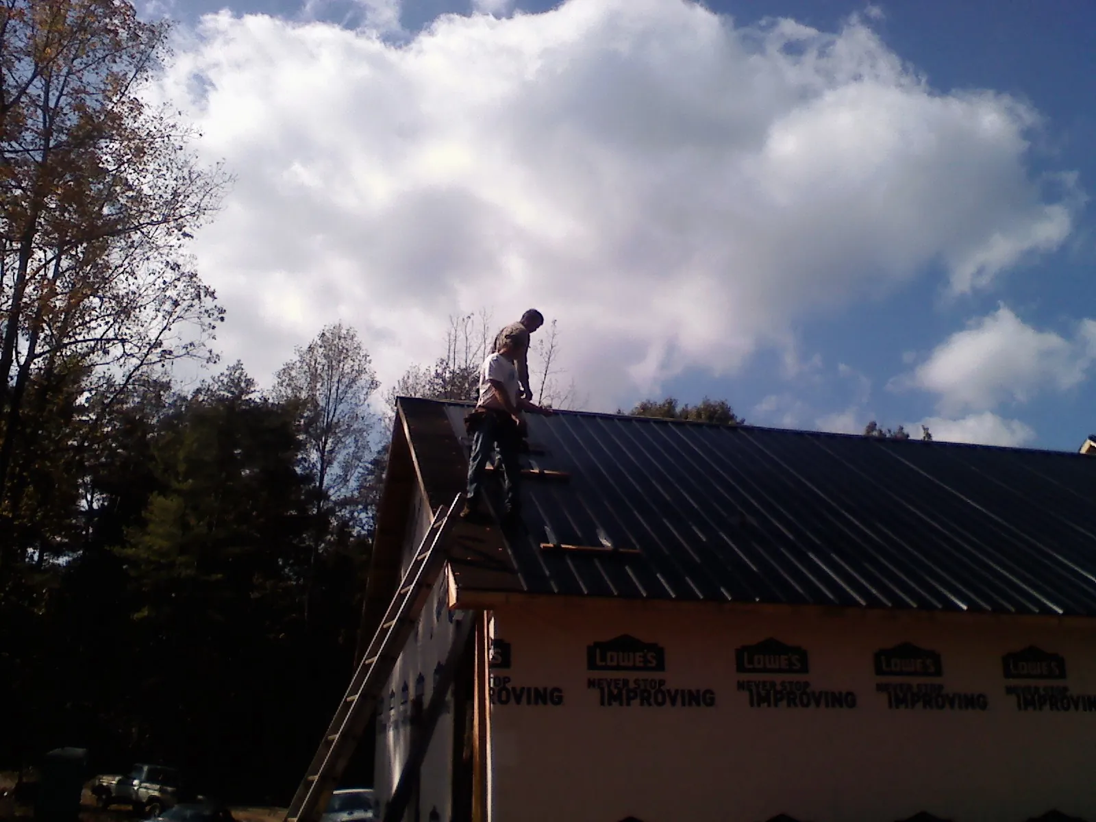 Roofer fastening dark metal panels high against a cloudy sky, from a Roof Inspection job in Painesville