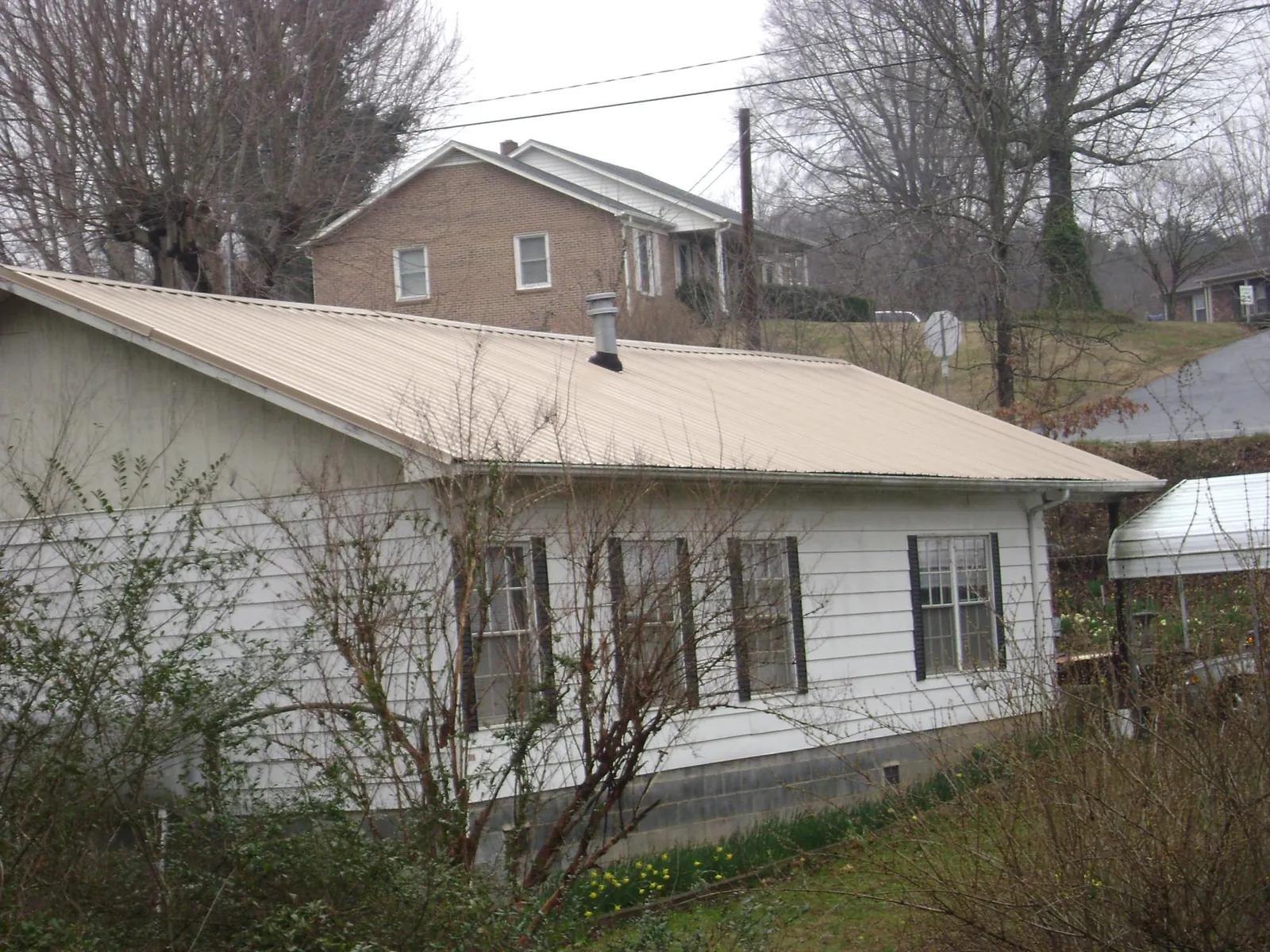 Tan metal roof on a white sided house set into a hillside — Commercial Roofing by Roofing Brothers in Painesville