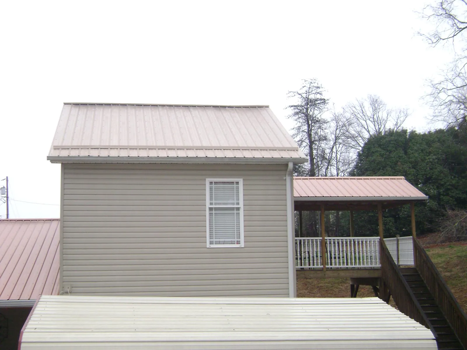 Tan metal roofs on a two story addition and attached porch, from a Roof Replacement job in Painesville